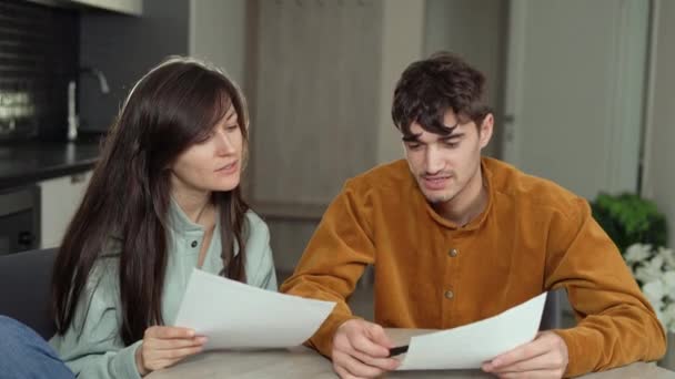 A man and a woman of are sitting at home in the kitchen. Carefully fill out the rental agreement — Stock Video