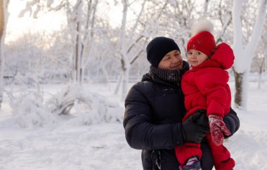 Genç beyaz bir adam kış parkında duruyor ve küçük kızını kollarına alıyor. Karlı kış ve aile. Metin için yer.
