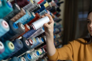 Kafkas uyruklu bir terzi dikiş atölyesinde duruyor ve kürsüye beyaz iplik koyuyor. İş yerinde bir terzi. Metnin için yer.