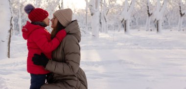 6 yaşındaki mutlu anne ve kızı kış karlı bir parkta sarılıyorlar. Aile ve çocukluk kavramı. Kışın çocuklar için eğlence..