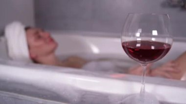 Bir bardak kuru kırmızı şarap küvetin kenarında duruyor, bir kadının eli kaldırıyor..