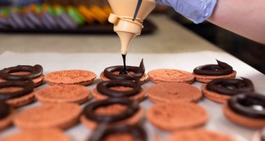 Makarnanın çikolata dolgusu şişeden dökülüyor. Dolguyla şişirilmiş kurabiye yapma süreci. Şeker hediye olarak..