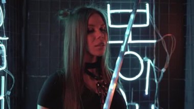 Genç beyaz kadın neon ışıklarda dans ediyor. Elinde bir kılıç tutuyor ve onunla hareket ediyor..