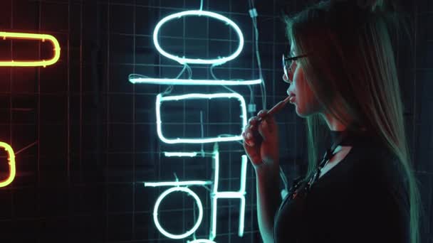 Silueta mladé krásné dívky stojí u lamp, kouří elektronickou cigaretu a vypouští kouř. Neonové světlo Nočního města — Stock video