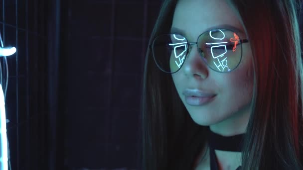Porträtt av en vit flicka i glasögon. Många neonreflektioner. Futuristisk modeannons med en ung kvinna. 4K — Stockvideo