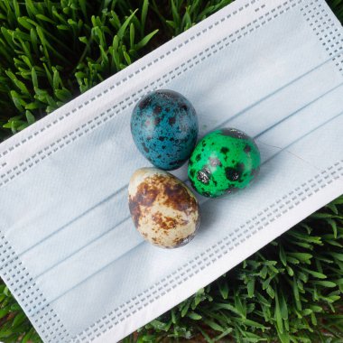 Birkaç parlak Paskalya yumurtası tıbbi bir maskenin üzerinde yatıyor. Pandemik ve Karantina sırasındaki tatil konsepti, Mutlu Paskalyalar.