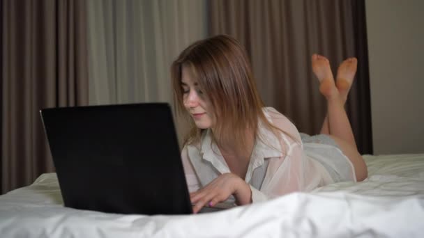 Portret pięknej kobiety leżącej w domu na łóżku i piszącej tekst na laptopie w sypialni. — Wideo stockowe