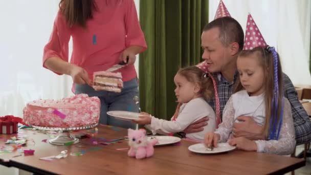 Keluarga ceria mengadakan pesta. Orang tua dan anak-anak bahagia merayakan ulang tahun mereka di dalam ruangan. putri menyajikan piring, ibu menempatkan kue. — Stok Video
