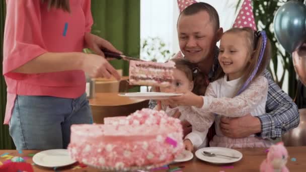 Una familia alegre dando una fiesta. Padres e hijos felices celebran su cumpleaños en el interior. hija sirve un plato, madre pone pastel. — Vídeo de stock