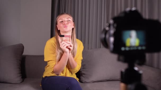 Kvinna skönhet bloggare skjuter hennes dagliga makeup tutorial på kameran på ett stativ. Den inflytelserika blondinen applicerar läppstift på läpparna live. Videostudio hemma — Stockvideo