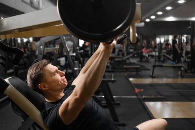 Simülatörde oturan genç bir beyaz erkek atlet kol ve göğüs kaslarını titretiyor. Bir sporcunun yakın çekimi. Üst vücudun kas gruplarının eğitimi.