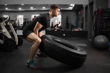 Modern bir spor salonunda güzel vücutlu yakışıklı beyaz bir sporcu egzersiz çarkını kaldırıyor. Ağırlık kaldırma yarışmasına hazırlanan bir sporcunun yan görünümü.