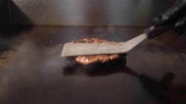 Peynirli burger için biftek ve domuz pirzolası pişiriyorum. Et mutfakta kızartılmış. Sulu et bir spatulayla ezilir..