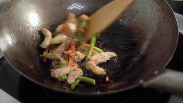 Matlagning garnering i en wok, asiatiska köket, grillning kyckling och grönsaker. Använd en spatel för att röra om i maten. snabbmatskoncept — Stockvideo