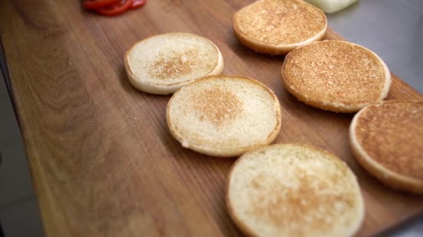 Produção de fast food. Há muitos rolos na mesa. Chef sufoca molho de queijo em um pão de hambúrguer. — Vídeo de Stock