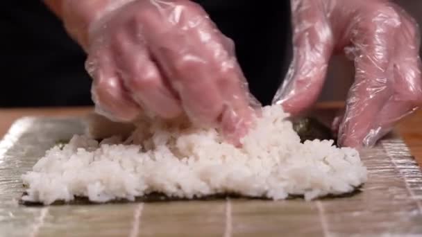 Preparar sushi en casa, primer plano de las manos de los chefs distribuir el arroz en una hoja nori. — Vídeos de Stock