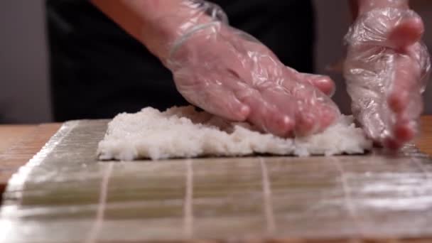 Preparar sushi en casa, primer plano de las manos de los chefs distribuir el arroz en una hoja nori. — Vídeos de Stock