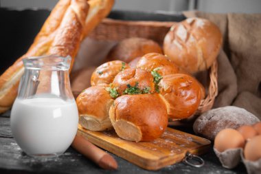 Pastane çeşitleri, sarımsaklı çörekler süt ve yumurtanın yanındaki mutfak tahtasının üzerinde. Boşluğu kopyala.