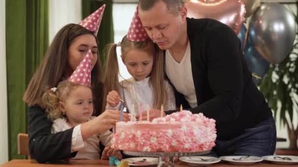 Vieren de verjaardag van een klein blank meisje in de familiekring. Papa houdt een lucifer vast en steekt kaarsen aan.. — Stockvideo