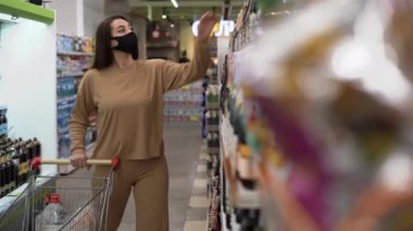 Koruyucu maskeli bir kadın süpermarkette şarap seçer. Karantina sırasındaki günlük yaşam. Sağlık hizmetleri ve koronavirüsten hastalıkların önlenmesi.