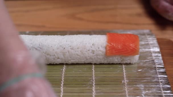 プロのシェフがスライスしたサーモンをキッチンテーブルの寿司ロールに追加します。日本料理店で鮭の寿司ロールを作る男性シェフ。. — ストック動画