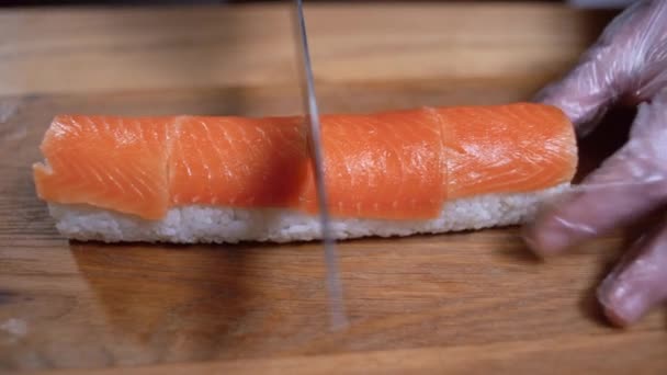 Las manos masculinas cortan el rollo de sushi de atún por la mitad en una tabla de cortar. Cortar rollos de sushi. — Vídeo de stock