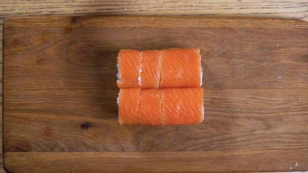 Vista superior As mãos masculinas cortam um rolo de sushi com salmão em várias partes em uma tábua de corte. Rolos de sushi de corte. — Vídeo de Stock