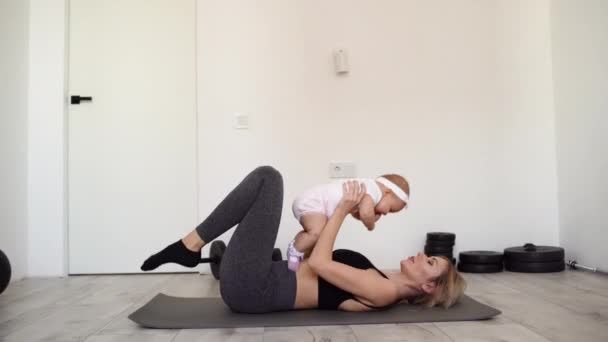 Mladá matka leží na podložce na jógu a cvičí spalování tuku. Silný trénink doma po porodu. Držet malou dceru v náručí — Stock video