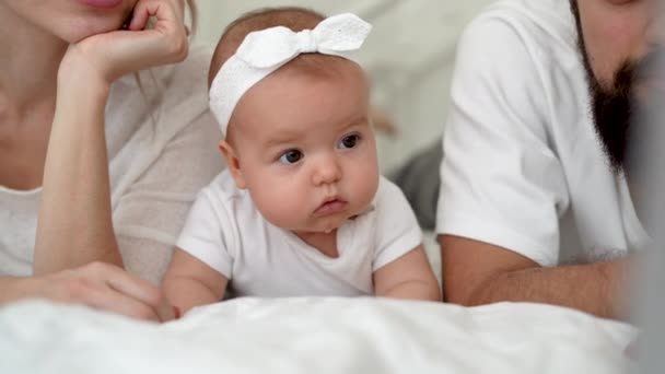 Porträtt av en glad ung familj med en liten flicka liggande på sängen. Helg tillsammans. Lycklig mor och far njuter av att uppfostra barn. flicka 4 månader — Stockvideo