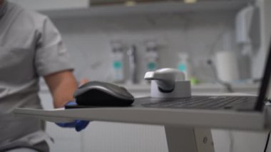 Dişleri taramak için dizüstü bilgisayarın yanındaki masada 3 boyutlu tarayıcı var. Doktor enstrümanı alır. 4k