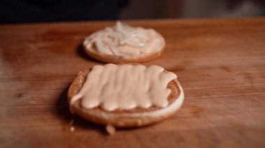 Profesyonel şef fast food restoranında lezzetli ve sulu hamburgerler hazırlıyor. Eldivenli bir şef hamburger ekmeğine lahana koyar..