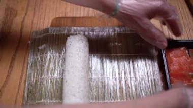 Profesyonel bir şef mutfak tezgahındaki karides suşisine dilimlenmiş somon ekliyor. Erkek bir şef bir Japon restoranında somon ve karides suşi rulosu hazırlıyor..