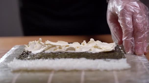 Близкая сцена процесса приготовления пищи. Шеф-повар готовит суши-рулеты. Он ложкой намазывает сливочный сыр на суши с нори.. — стоковое видео