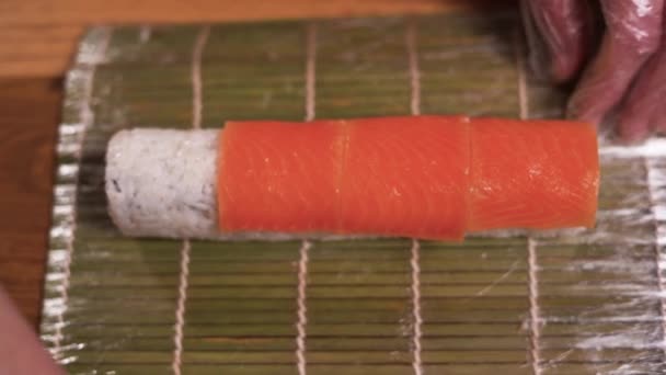 A professional chef adds sliced salmon to a sushi roll on the kitchen table. A male chef prepares a salmon sushi roll at a Japanese restaurant. — Stock Video