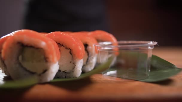 El chef coloca el wasabi en un recipiente de plástico desechable en un juego de sushi maki, luego vierte la salsa sobre el maki. Deliciosa comida japonesa para llevar. Presentación menú restaurante. — Vídeo de stock