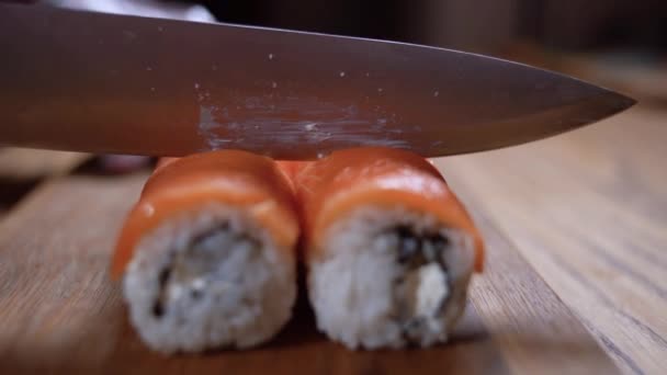 Mãos masculinas cortam o rolo de sushi de salmão em vários pedaços em uma tábua de corte. Rolos de sushi de corte. — Vídeo de Stock