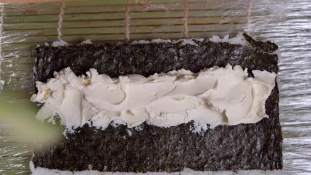 Gros plan sur la cuisson. Le chef prépare des rouleaux de sushi. Il a mis du concombre sur du fromage à la crème, des sushis nori. — Video