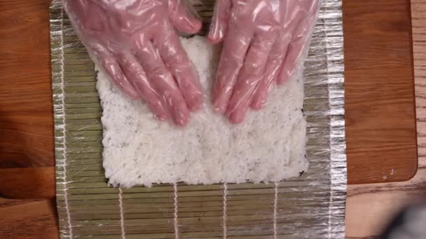 Cooking at home, top view hands of the chef distribute boiled rice on sushi nori leaf. — Stock Video