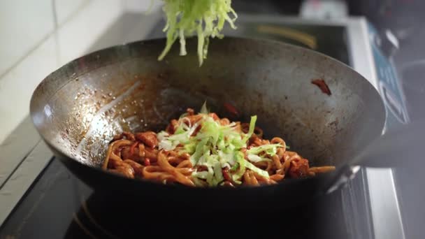 A female chefs hand throws Chinese cabbage onto a hot wok with noodles. — Stock Video