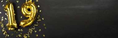 19 numaralı altın folyo balonu. 19. yazılı doğum günü veya yıldönümü tebrik kartı. Siyah beton arka plan. Yıldönümü kutlaması. Pankart. Boşluğu kopyala