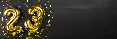 Altın folyo balonu 23 numara. 23 yazısıyla birlikte doğum günü veya yıldönümü tebrik kartı. Siyah beton arka plan. Yıldönümü kutlaması. Pankart. Boşluğu kopyala