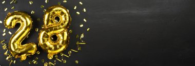 28 numaralı altın folyo balonu. 28 yazılı doğum günü veya yıldönümü tebrik kartı. Siyah beton arka plan. Yıldönümü kutlaması. Pankart. Boşluğu kopyala