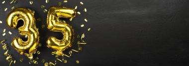 35 numaralı altın folyo balonu. 35 yazılı doğum günü ya da yıldönümü kartı. Siyah beton arka plan. Yıldönümü kutlaması. Pankart. Boşluğu kopyala