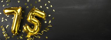 75 numaralı altın folyo balonu. Doğum günü ya da yıldönümü kartında 75 yazılıydı. Siyah beton arka plan. Yıldönümü kutlaması. Pankart. Boşluğu kopyala