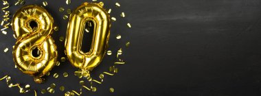 Seksen numaralı altın folyo balonu. 80 yazılı doğum günü ya da yıldönümü kartı. Siyah beton arka plan. Yıldönümü kutlaması. Pankart. Boşluğu kopyala