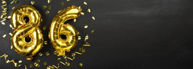 86 numaralı altın folyo balonu. 86 yazılı doğum günü ya da yıldönümü kartı. Siyah beton arka plan. Yıldönümü kutlaması. Pankart. Boşluğu kopyala
