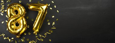 87 numaralı altın folyo balonu. 87 yazılı doğum günü ya da yıldönümü kartı. Siyah beton arka plan. Yıldönümü kutlaması. Pankart. Boşluğu kopyala