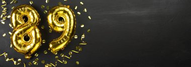 Seksen dokuz numaralı altın folyo balonu. 89 yazılı doğum günü ya da yıldönümü kartı. Siyah beton arka plan. Yıldönümü kutlaması. Pankart. Boşluğu kopyala