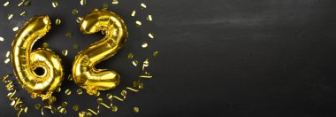 Altmış iki numaralı altın folyo balonu. Doğum günü ya da yıldönümü kartında 62 yazılıydı. Siyah beton arka plan. Yıldönümü kutlaması. Pankart. Boşluğu kopyala