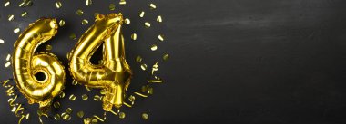 Altmış dört numaralı altın folyo balonu. Doğum günü ya da yıldönümü kartında 64 yazılıydı. Siyah beton arka plan. Yıldönümü kutlaması. Pankart. Boşluğu kopyala
